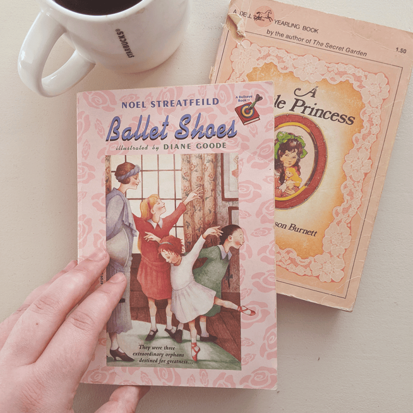 Bookstagram photo featuring BALLET SHOES by Noel Streatfeild and A LITTLE PRINCESS by Frances Hodgson Burnett. The books are laid on a white surface next to a mug of coffee. Elza's hand rests gently on the cover.